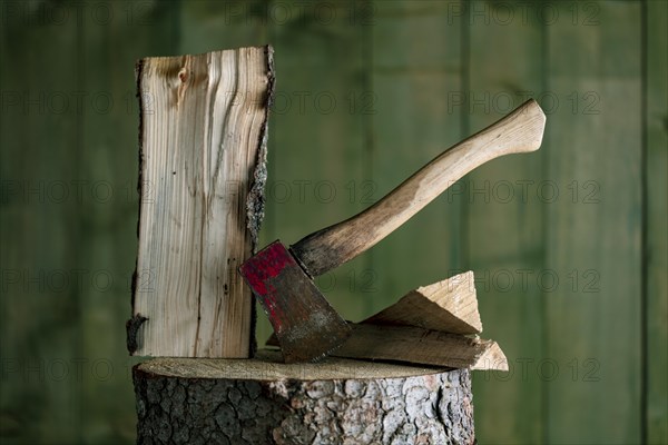 Axe on chopping block with log in front of green wooden wall, studio shot, Germany, Europe