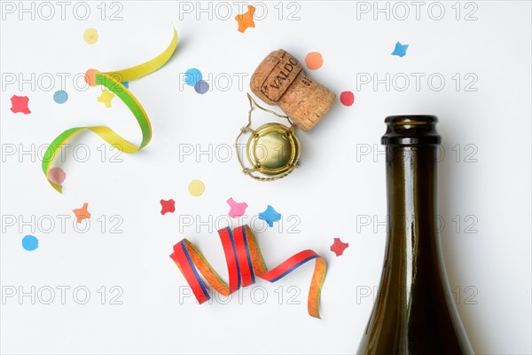 Champagne bottle, champagne cork, streamers and confetti against a white background