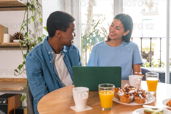 Multi-ethnic couple making online purchase with computer while having breakfast