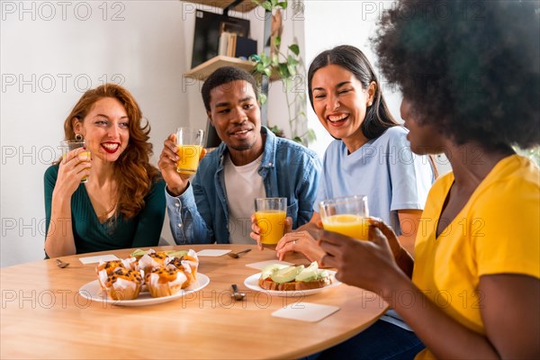 Multiethnic friends having fun at a breakfast with orange juice and muffins at home