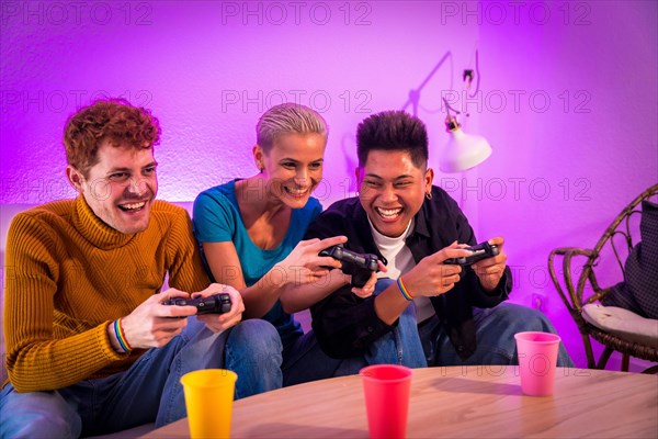 Group of young friends playing video games together on the sofa at home, purple led, having fun