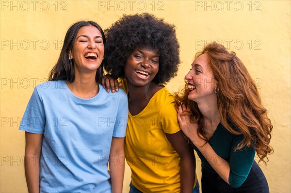 Portrait of beautiful multiethnic female friends smiling on a yellow wall having fun