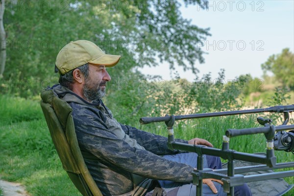 Fisherman with beard and cap sitting on a chair waiting for a fish to catch a bite
