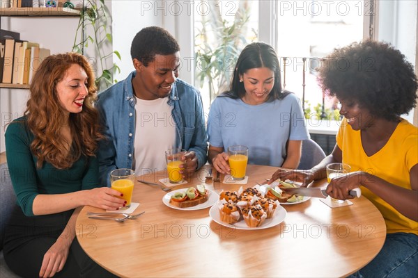 Multi-ethnic friends at a breakfast with orange juice and muffins at home, cutting the toasts