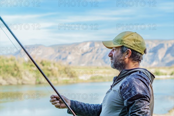 Man with beard and cap preparing his fishing gear on the river bank