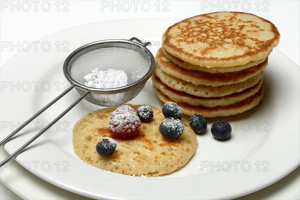 Blini, stacked blinis and sieve with icing sugar, fruit, mini pancakes