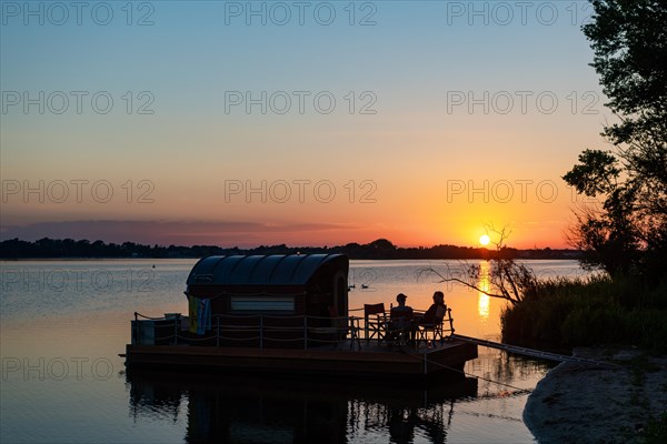 Two men sitting on a houseboat at sunset, house raft, in front of the island Kiehnwerder, Breitlingsee, Brandenburg an der Havel, Havelland, Brandenburg, Germany, Europe