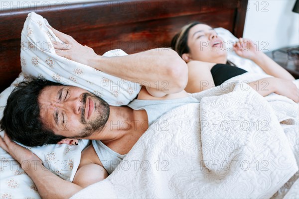 Woman snoring in bedroom and husband covering his ears. Husband suffering from the snoring of his sleeping wife. Sleep apnea concept