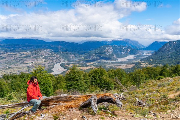Hiker taking a break on a tree trunk, ascent to the lagoon on Cerro Castillo mountain, the river valley of the Rio Ibanez in the background, Cerro Castillo National Park, Aysen, Patagonia, Chile, South America