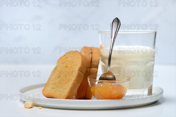 Rusk, glass of milk and orange marmalade in small bowls