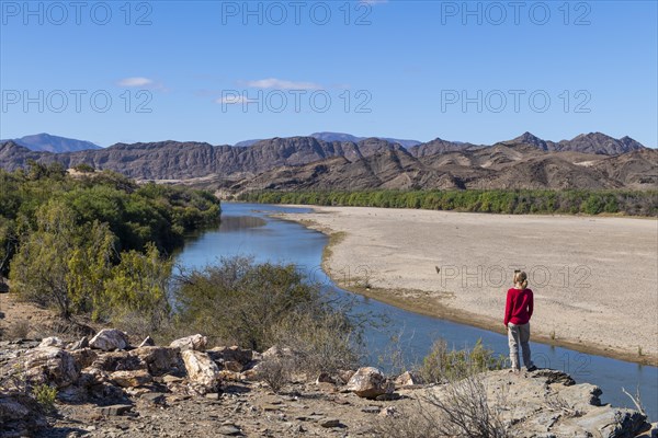 Woman standing on the Orange River, also known as the Orange River, on the border between Namibia and South Africa, Oranjemund, Sperrgebiet National Park, also known as Tsau ÇKhaeb National Park, Namibia, Africa
