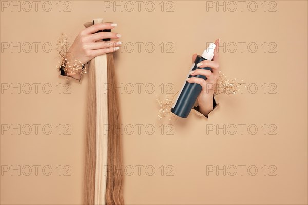 Hands with flowers hold strands of hair for extensions on a beige background. hair beauty