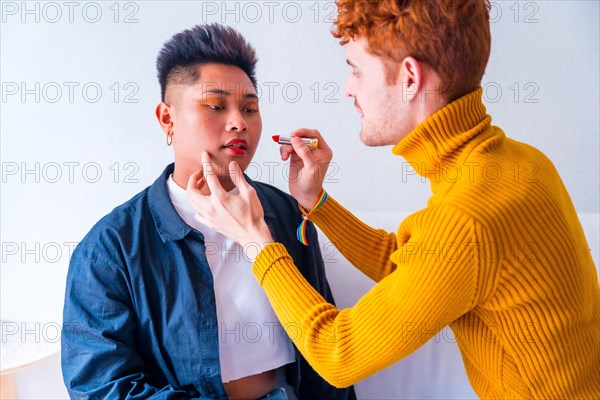 Beautiful gay couple putting on makeup painting their lips being romantic indoors at home, lgbt concept