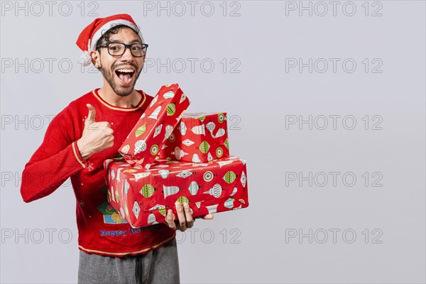 Smiling guy in christmas hat holding christmas gift boxes giving thumbs up. Friendly man in christmas clothes holding gift boxes, Christmas man holding gift boxes and smiling with thumb up