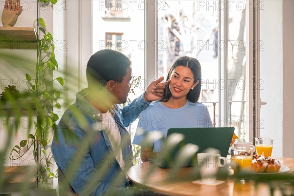 Couple in love making purchase online with the computer while having breakfast, next to the window