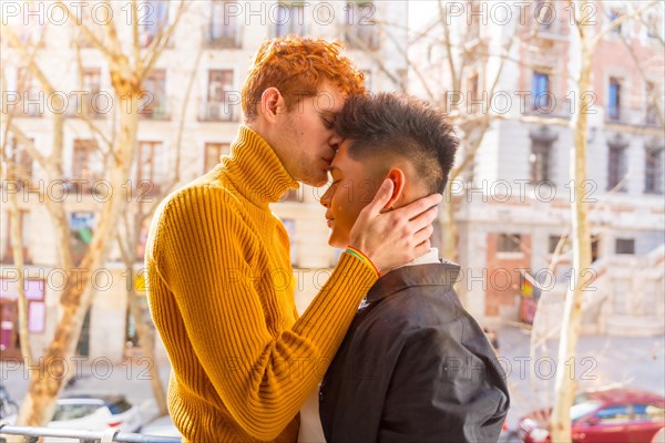 Beautiful gay couple being romantic at home on the sofa, home balcony kissing each other on the forehead, lgbt concept