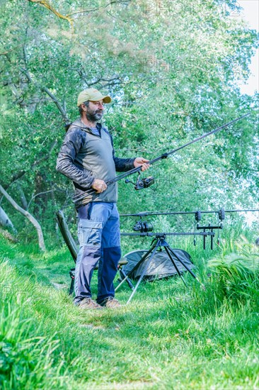 Bearded fisherman setting up his fishing gear on the river bank on a green grass field