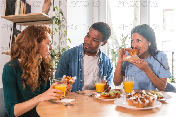 Friends at a breakfast with orange juice and muffins at home, having fun in the morning