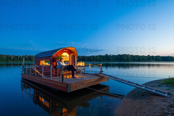 Man sitting in the blue hour on a houseboat, house raft, in front of the island Kiehnwerder, Breitlingsee, Brandenburg an der Havel, Havelland, Brandenburg, Germany, Europe