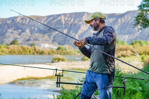 Man with beard and cap preparing his fishing gear on the river bank