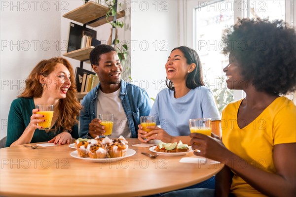 Multiethnic friends having breakfast with orange juice and muffins at home