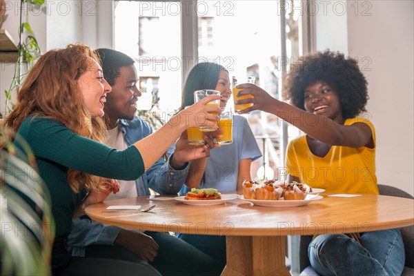 Multi-ethnic friends toasting over breakfast with orange juice and muffins at home