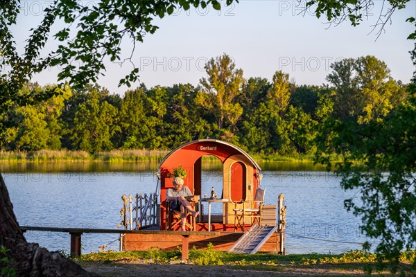 Man sitting on a houseboat, house raft, in front of the island Kiehnwerder, Breitlingsee, Brandenburg an der Havel, Havelland, Brandenburg, Germany, Europe