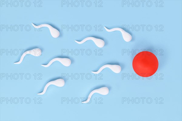 Abstract sperm cells swimming towards egg cell on blue background