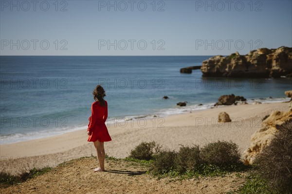 Attractive woman in red dress on top of cliffs at Sao Rafael Beach, Algarve coast, Portugal, Europe