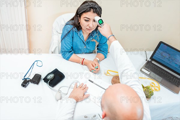 Male doctor taking temperature with gun to patient. Doctor measuring temperature with infrared gun to female patient, Doctor taking temperature to woman patient in office