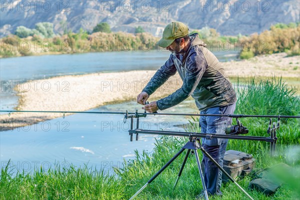 Male angler preparing on the river for a day of carpfishing, setting up the rods on the stand