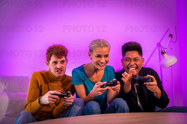 Group of young friends playing video games together on the sofa at home, purple led, having fun pushing