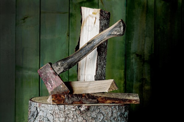 Axe on chopping block with log in front of green wooden wall, studio shot, Germany, Europe