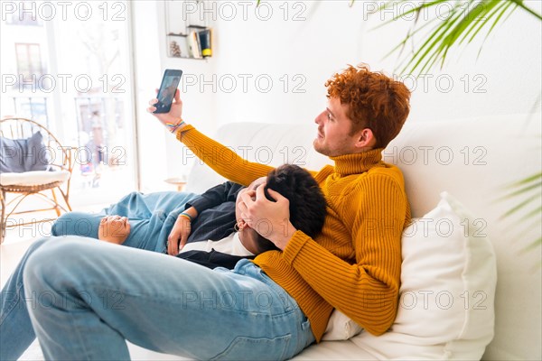 Beautiful gay couple being romantic indoors at home on the sofa, gay couple taking selfie, lgbt concept