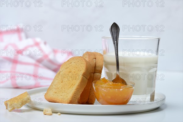 Rusk, glass of milk and orange marmalade in small bowls