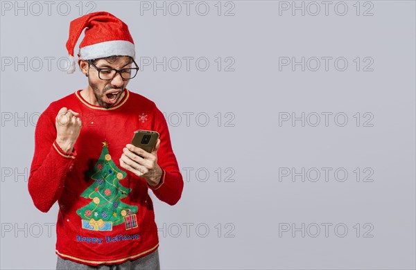 Excited guy in christmas hat looking at cellphone and celebrating. People in santa hat looking at cell phone excited, Excited young man in christmas hat using cellphone celebrating