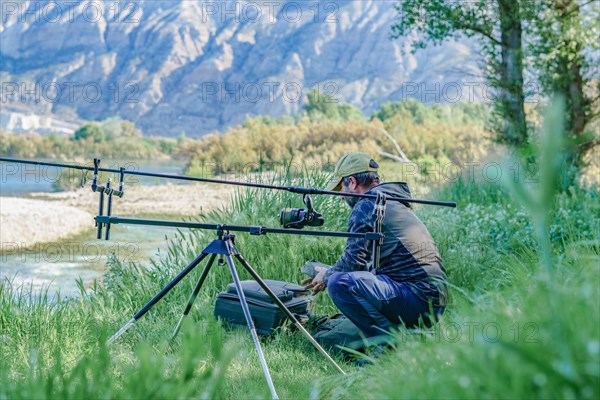 Male angler preparing on the river for a day of carpfishing, setting up the rods on the stand