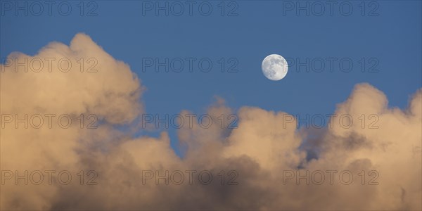 Rising full moon in the evening sky with reddish clouds