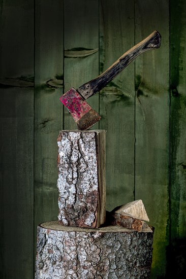 Axe on chopping block with log in front of green wooden wall, studio shot, Germany, Europe