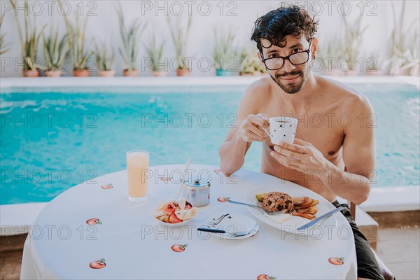 Breakfast near the swimming pool. Young man on vacation in hotel having breakfast near swimming pool. Person having breakfast in the hotel with pool in the background
