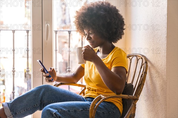Afro hair woman by the window home having a hot drink, coffee in the morning