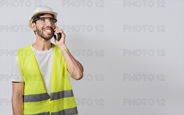 Young builder engineer in vest talking on cell phone isolated. Civil engineer concept talking on cellphone isolated, Smiling engineer talking on the phone isolated with copy space