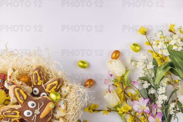 Colourfully decorated Easter biscuits in a nest, spring flowers, chocolate eggs, white background