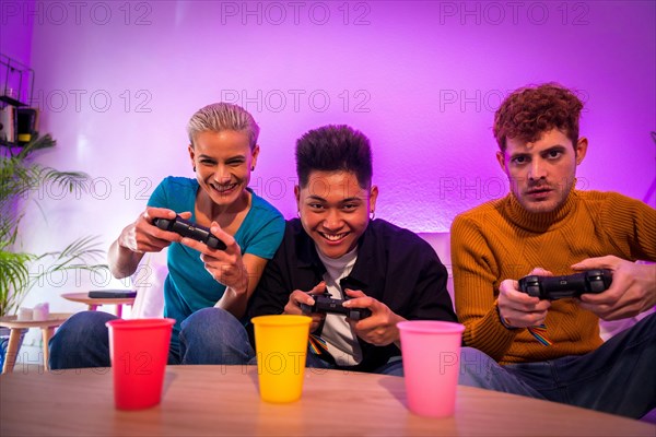 Group of young friends playing video games together on the sofa at home, portrait looking at camera