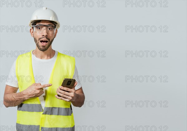 Engineer using and pointing at cellphone. Amazed construction worker using and pointing cellphone. Surprised face engineer using cell phone. Construction engineer pointing at phone promo