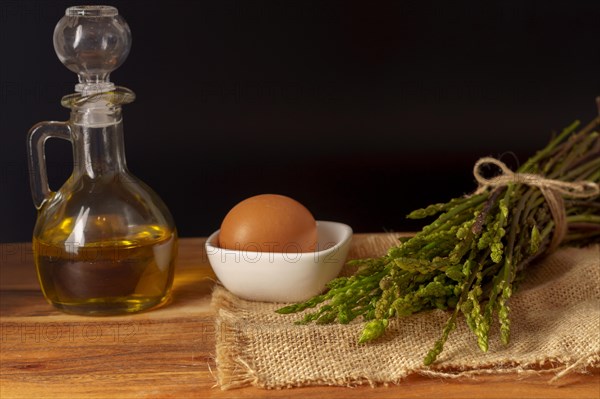 Bunch of wild asparagus on a raffia cloth with a jar of olive oil and eggs black background