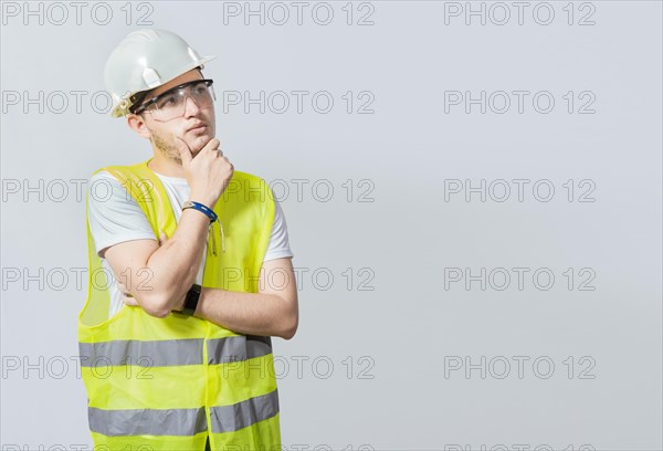 A pensive engineer on white background. Concept of a meditative engineer solated. Pensive builder man with hand on chin, Portrait of young builder thinking with hand on chin isolated