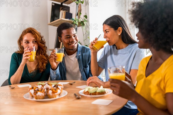 Multiethnic friends having fun at a breakfast with orange juice and muffins at home