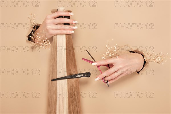 Hands with flowers hold strands of hair for extensions on a beige background. hair beauty