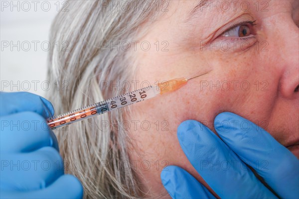 Close-up of a cosmetologists hands injecting botox into the face of an older woman with wrinkles